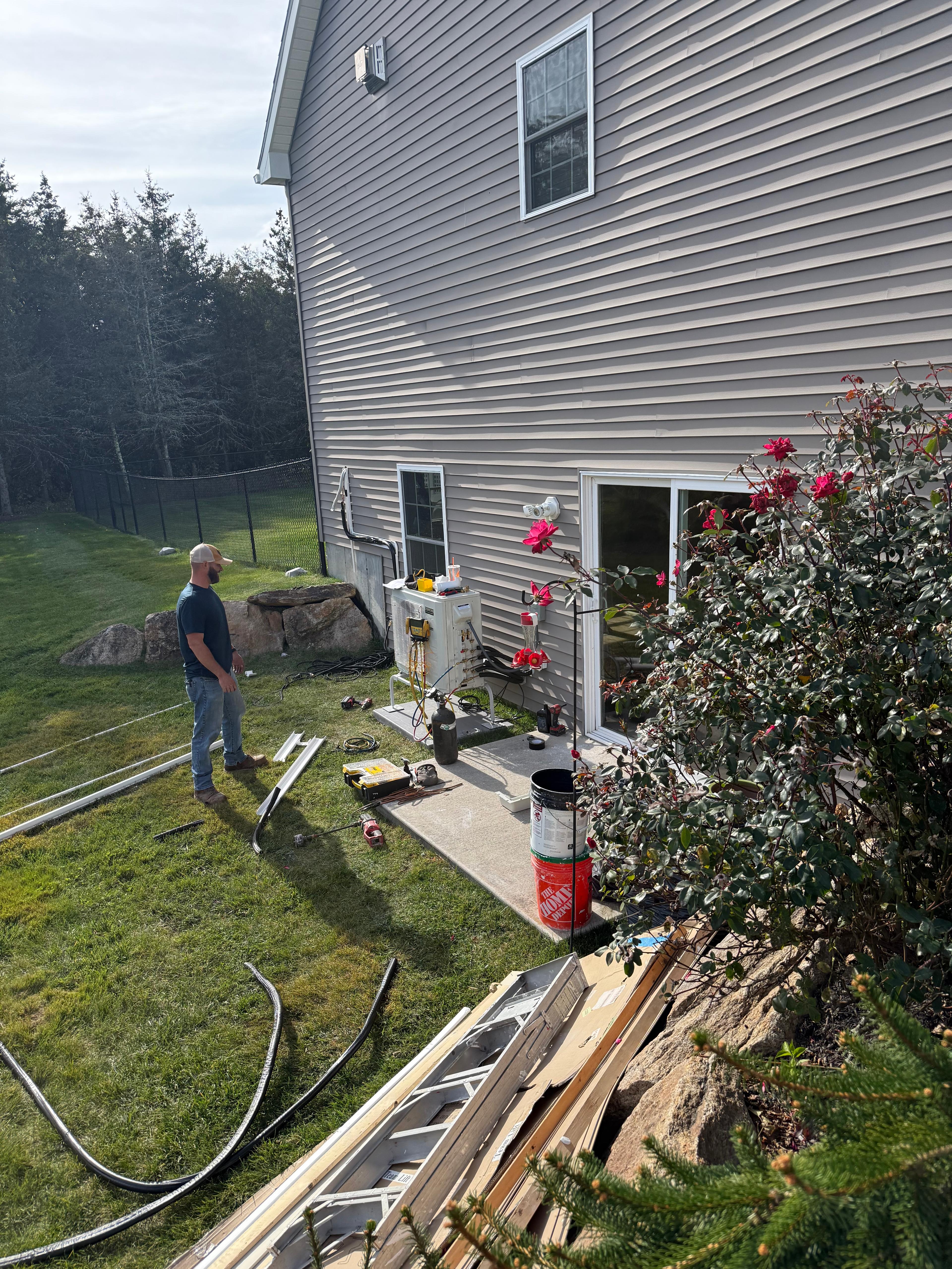 HVAC technician working on outdoor equipment beside a residential home