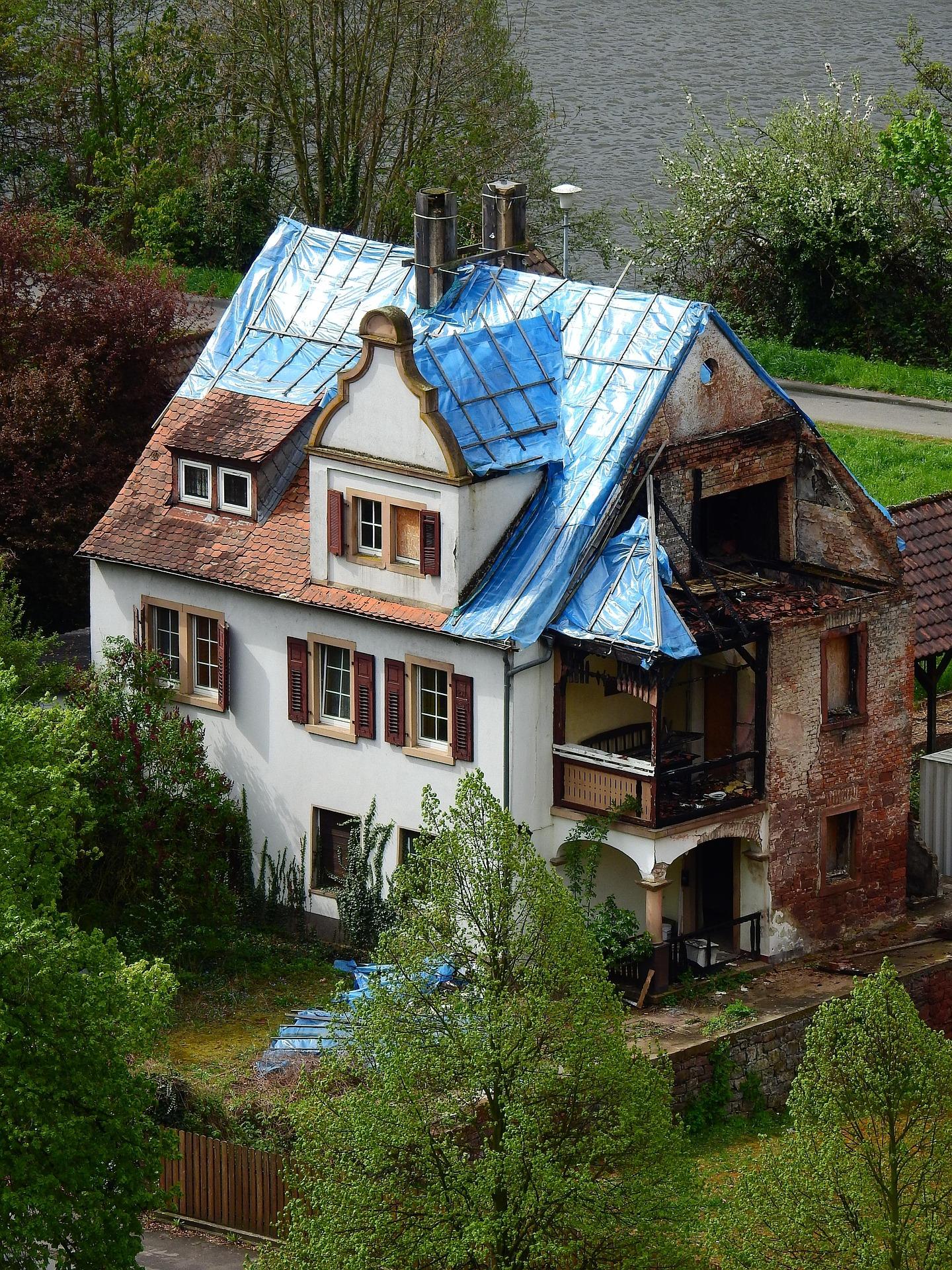 Older house with blue tarp on roof awaiting renovation